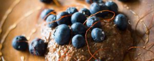 Le pudding à la myrtille de graines de chia est servi sur une planche à découper en bois avec des myrtilles entières et du sirop d'agave. Les fils de piment donnent un effet de fête.