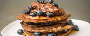 Stapel pancakes overladen met bosbessen en een topping van chocolade en kokosbloesemsuiker